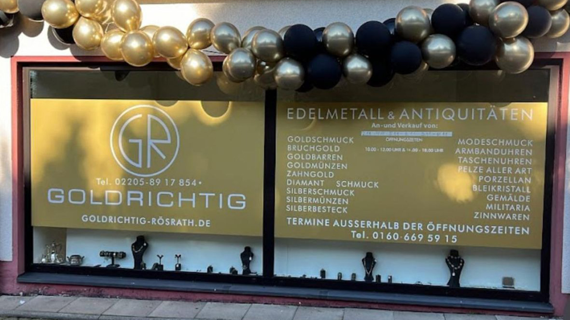 Schaufenster eines Geschäfts mit goldener Werbefläche, schwarzer und goldener Ballongirlande und Auflistung verschiedener Edelmetallprodukte