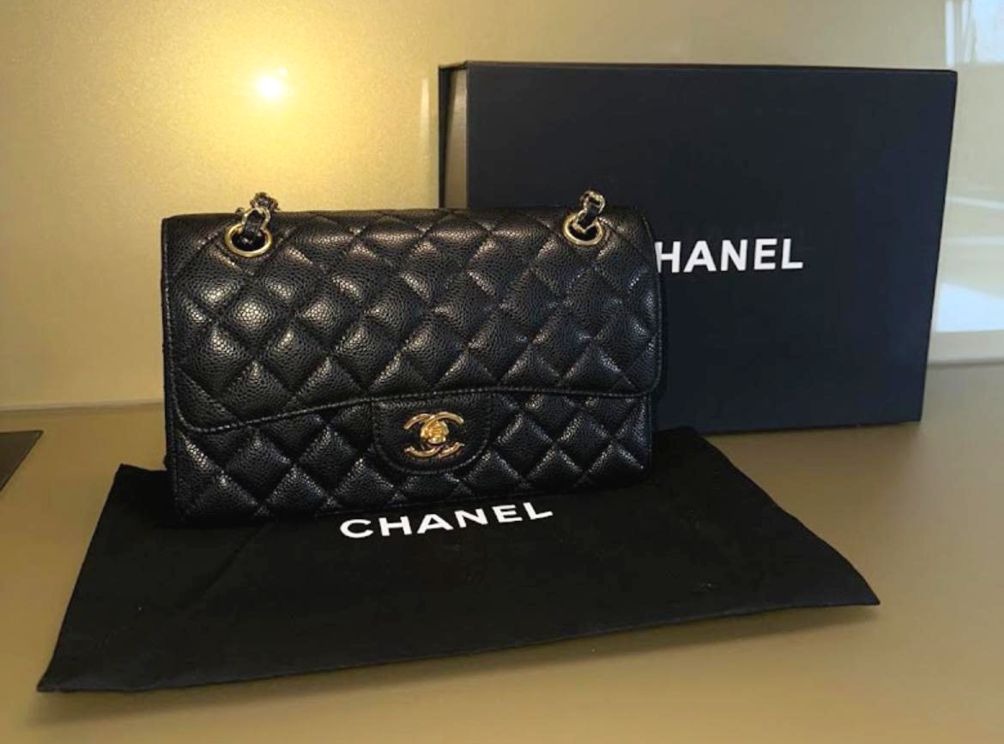 Eine schwarze gesteppte Chanel Tasche mit Goldketten liegt vor einer Chanel Box
